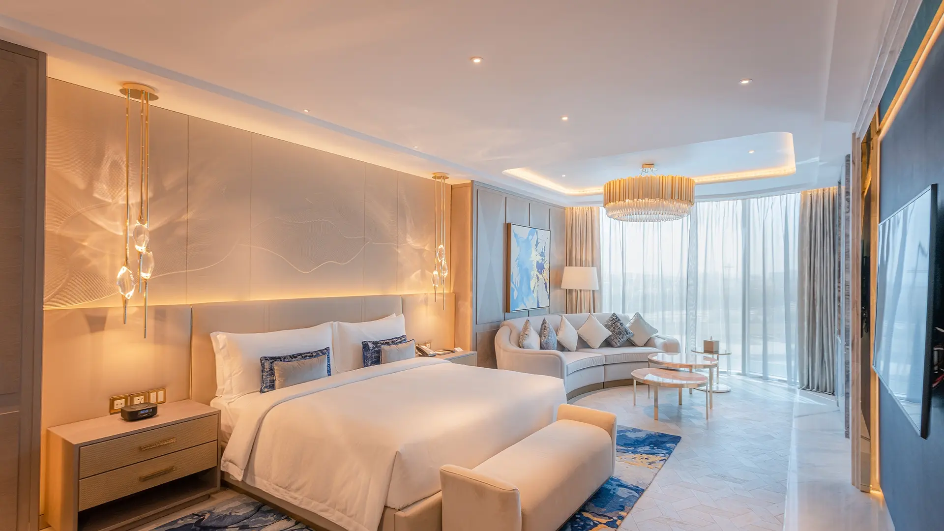Hotel suite with a panelled bed wall, pendant lights and a lounge area